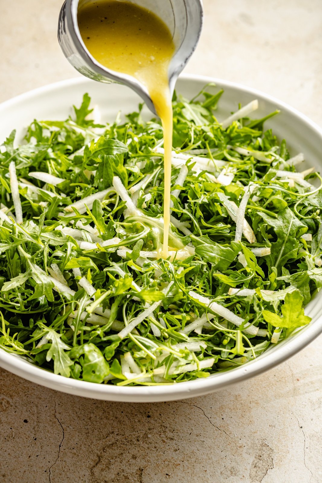 pouring dressing onto an arugula pear salad in a bowl