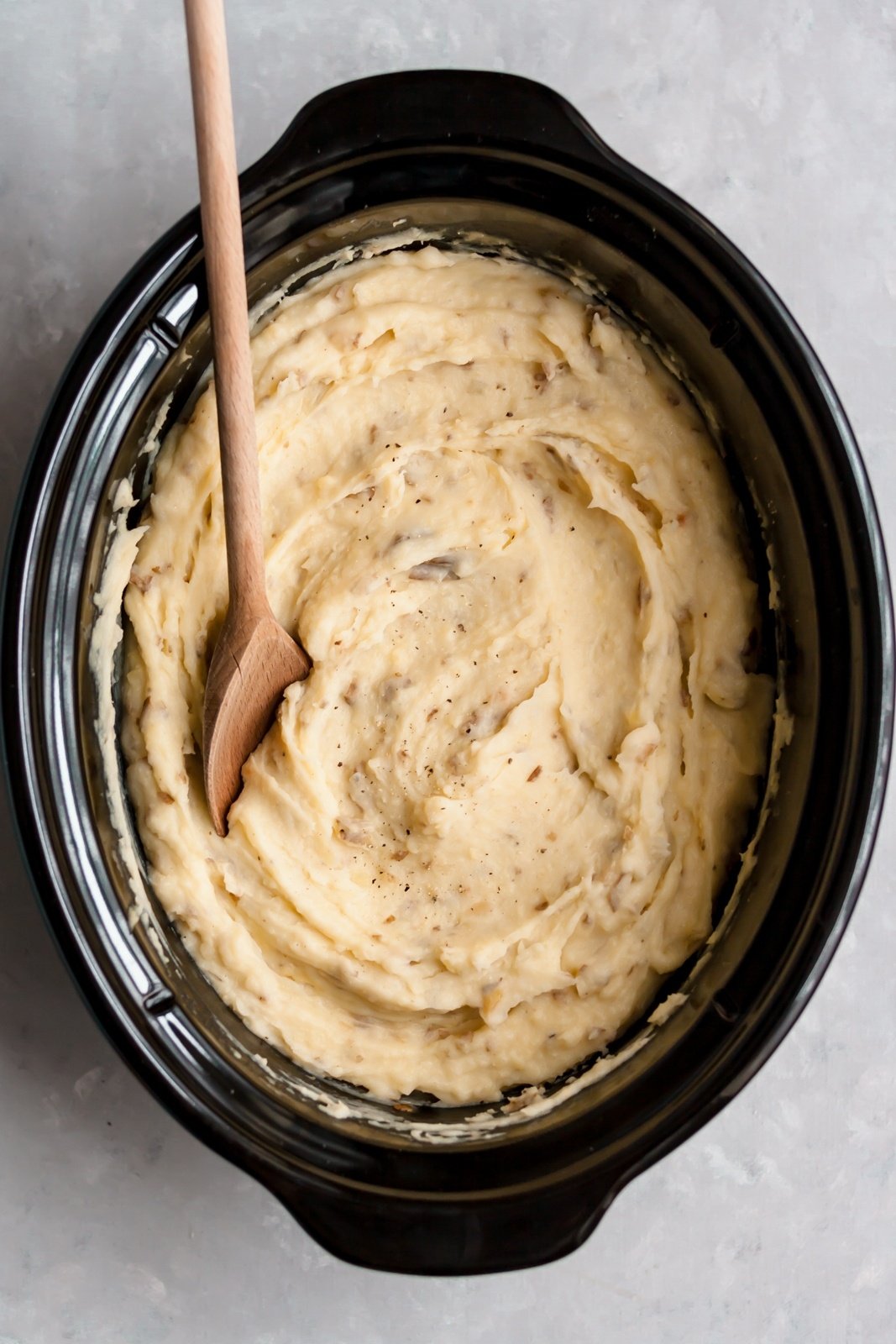 crock pot mashed potatoes in the bowl of a crock pot with a wooden spoon