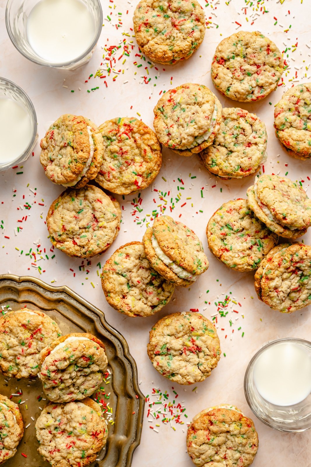 christmas sandwich cookies on a table next to glasses of milk