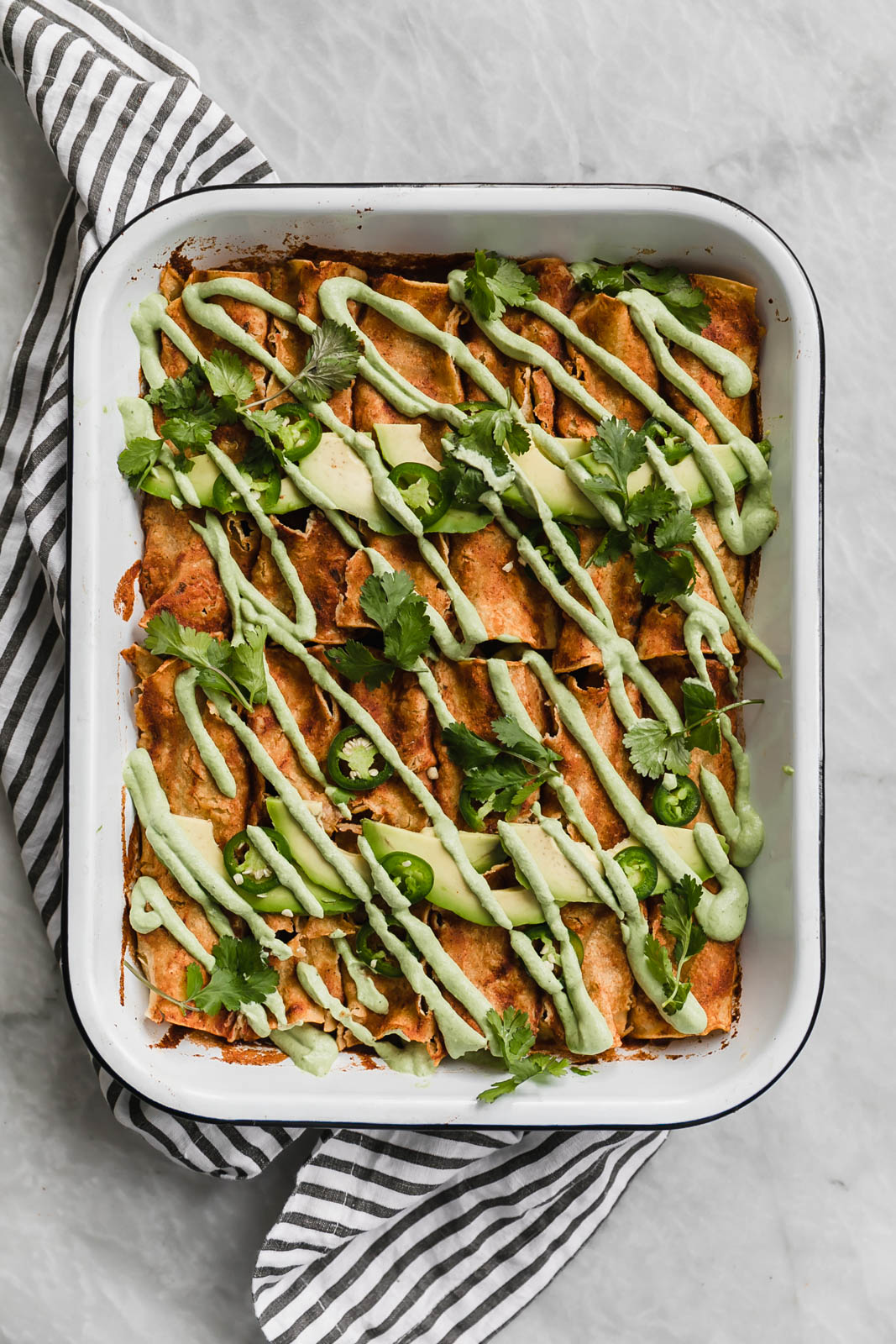 vegan enchiladas in a pan drizzled with jalapeño cashew crema