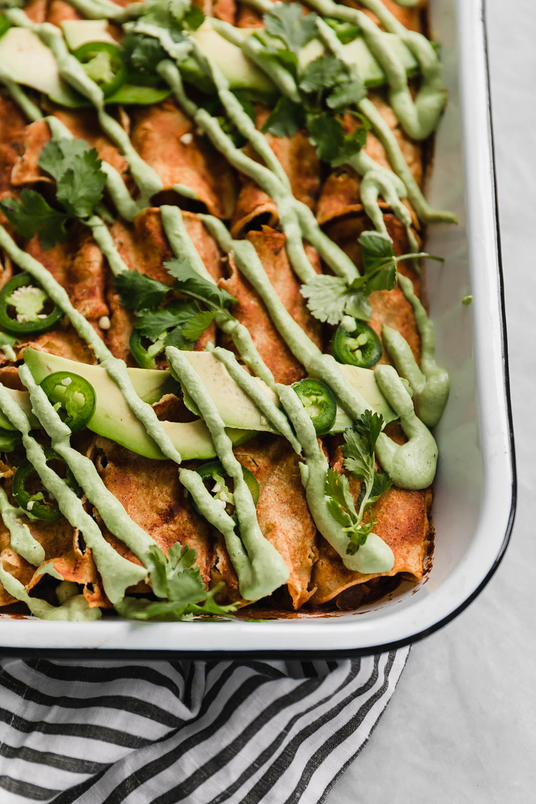 vegan black bean enchiladas in a pan drizzled with jalapeño cashew crema