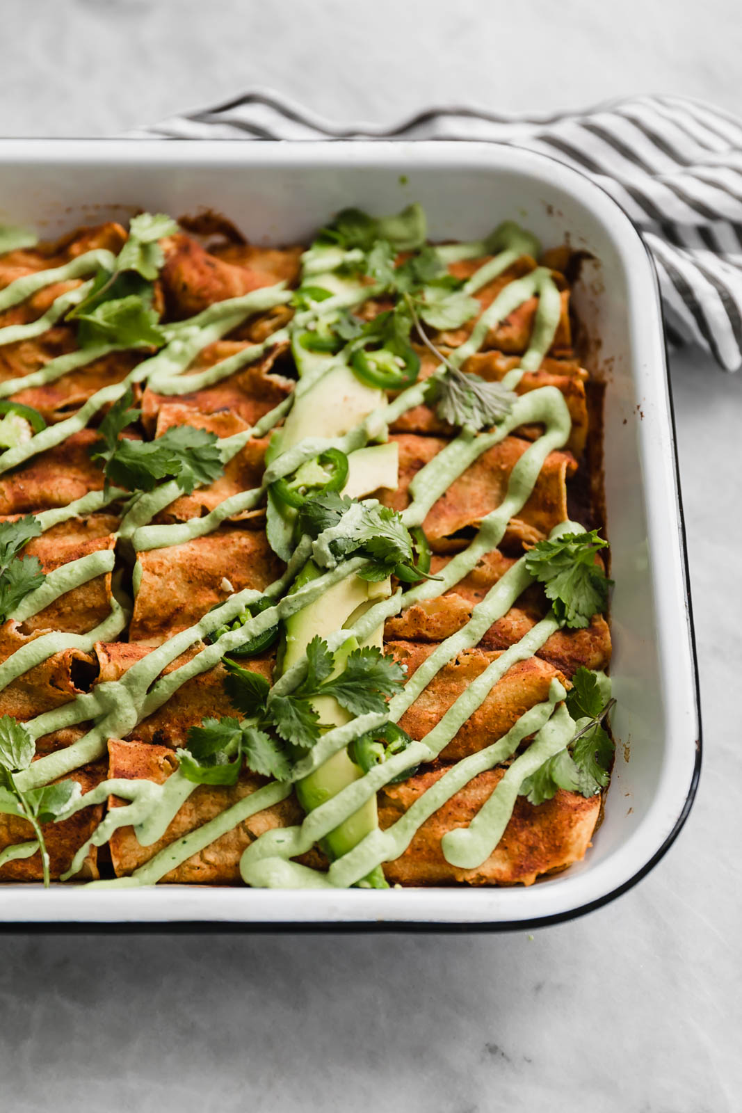 vegan enchiladas in a pan drizzled with jalapeño cashew crema