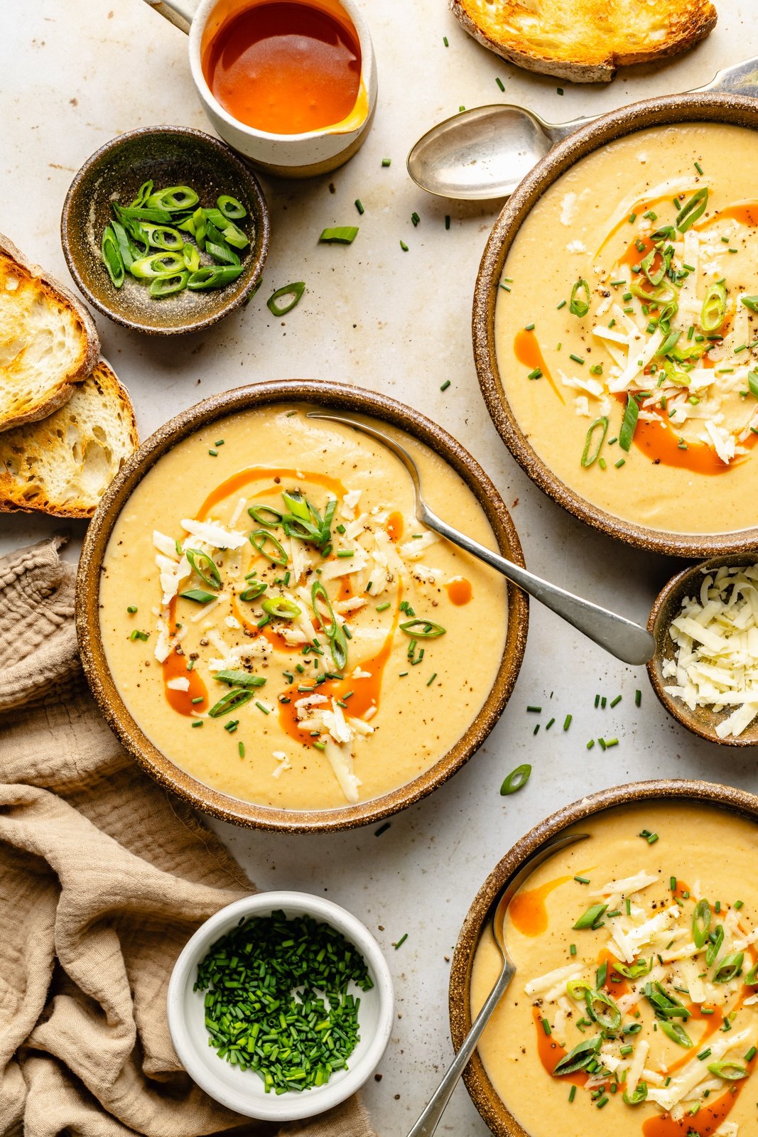 creamy buffalo cauliflower soup in bowls next to bowls of herbs