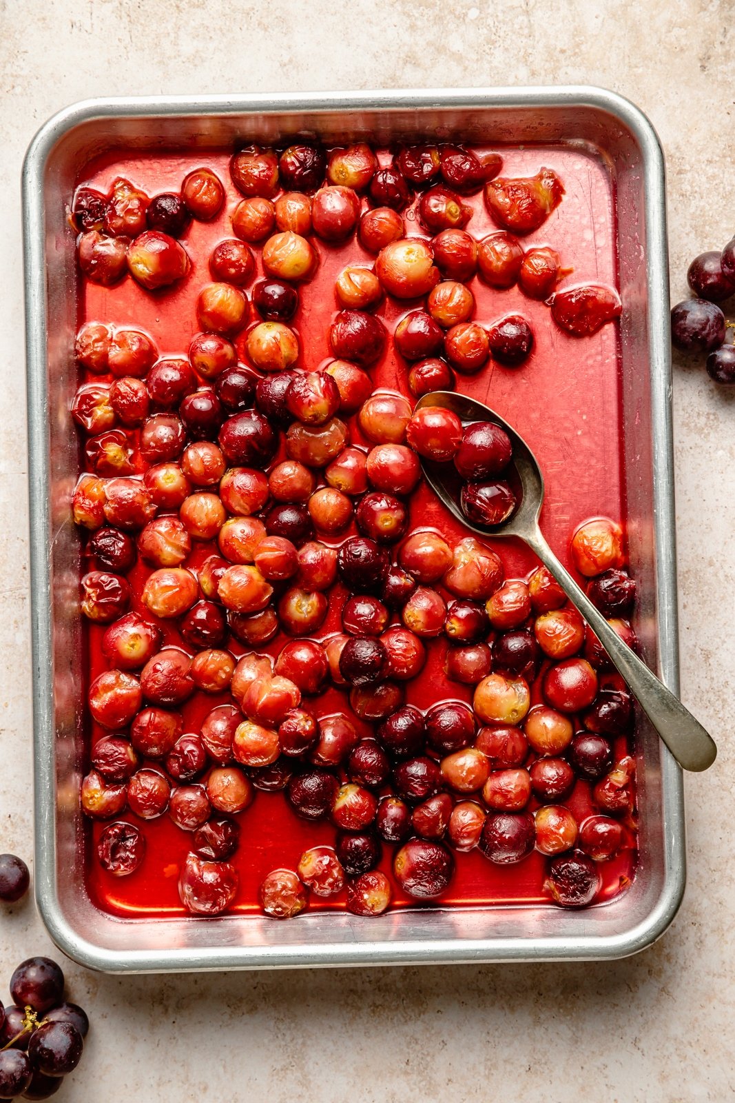 roasted grapes on a baking sheet with a spoon