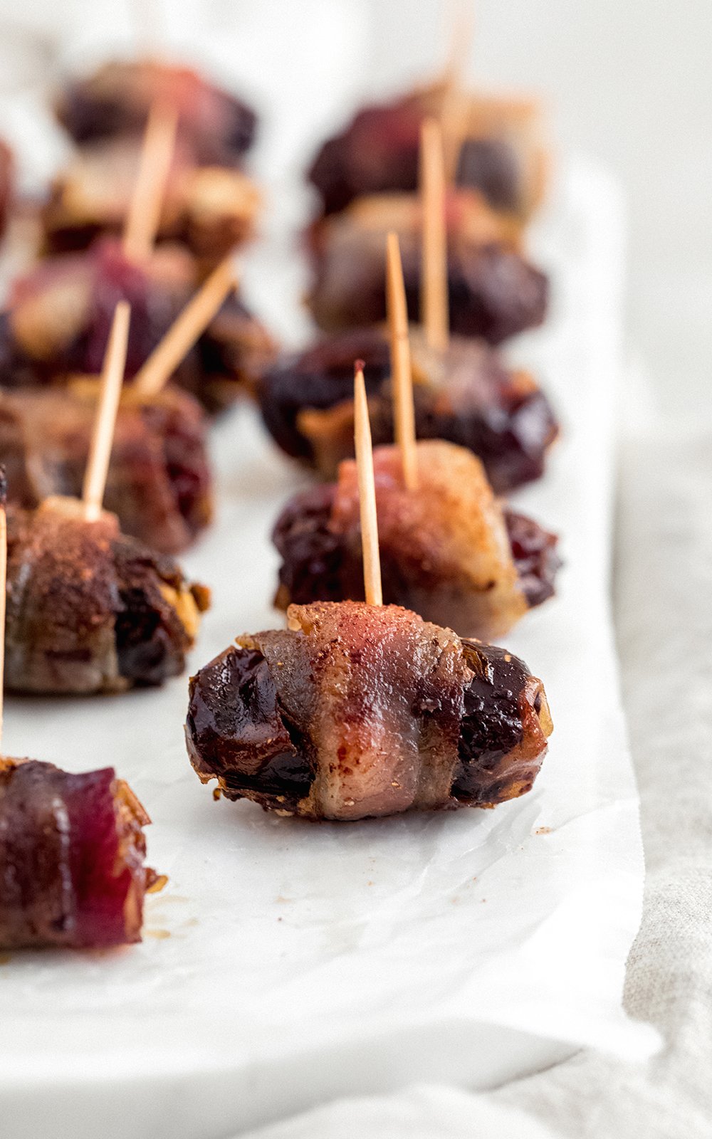 bacon wrapped dates with toothpicks on parchment paper