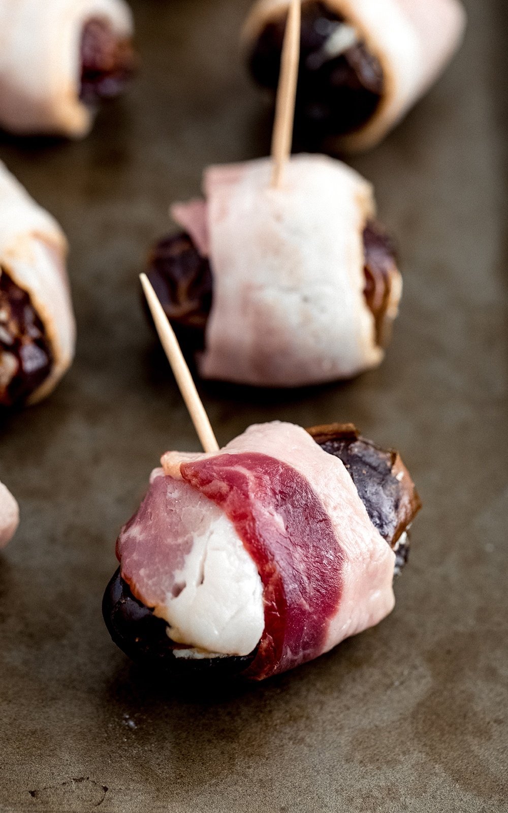 bacon wrapped dates with toothpicks on a baking sheet